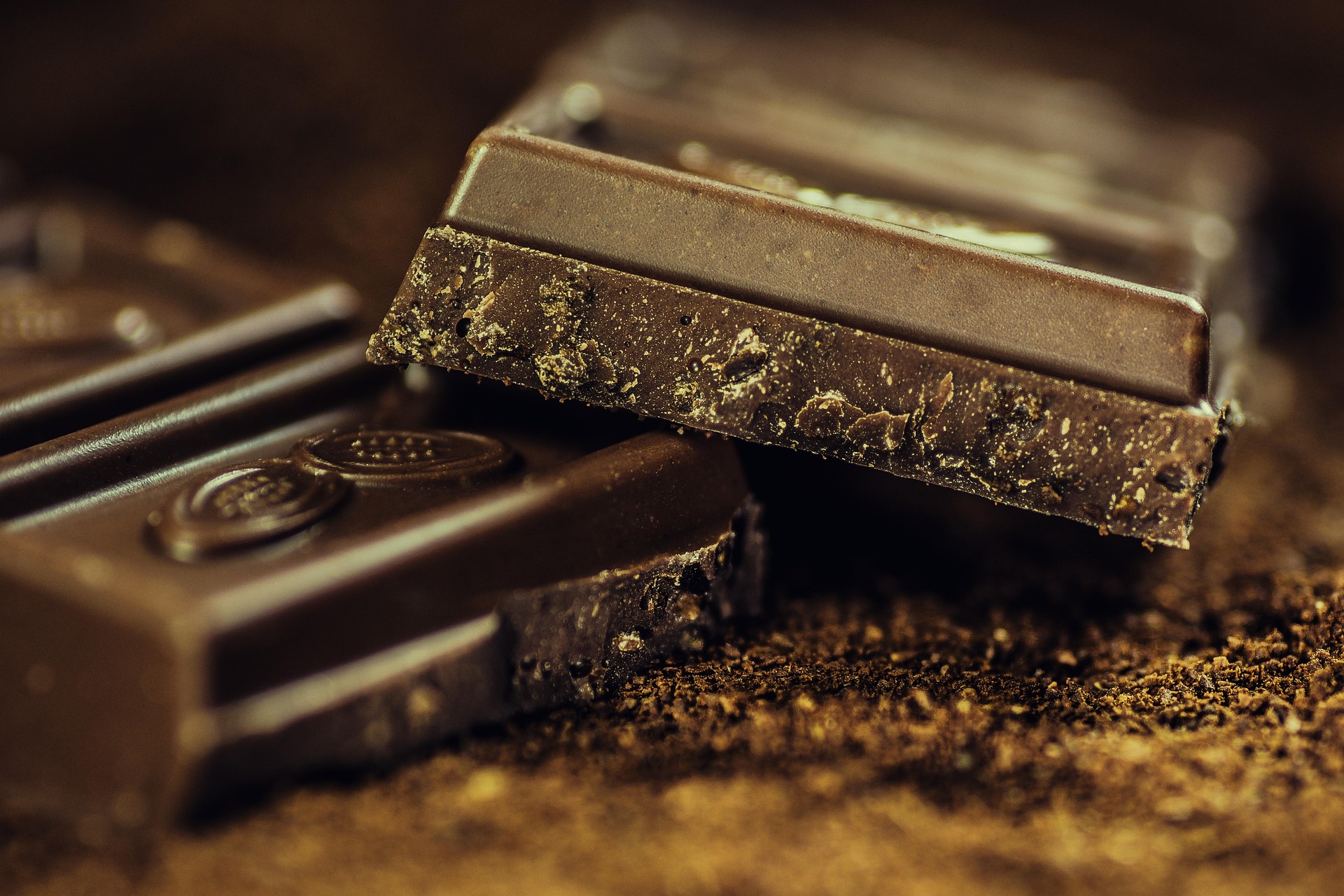 Tablettes de chocolat noir avec éclats en gros plan, posées sur une surface saupoudrée de cacao.